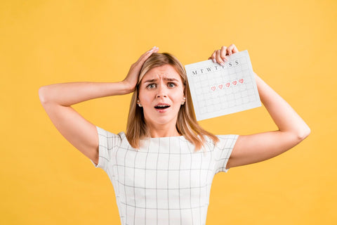 mujer con una mano en la cabeza y sosteniendo un calendario preocupada